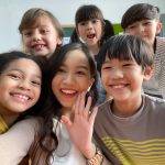 Smiling young Asian teacher making selfie with her schoolchildren in classroom.